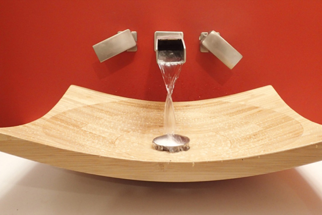 A wall-mounted tap running into a wooden basin in a finished bathroom